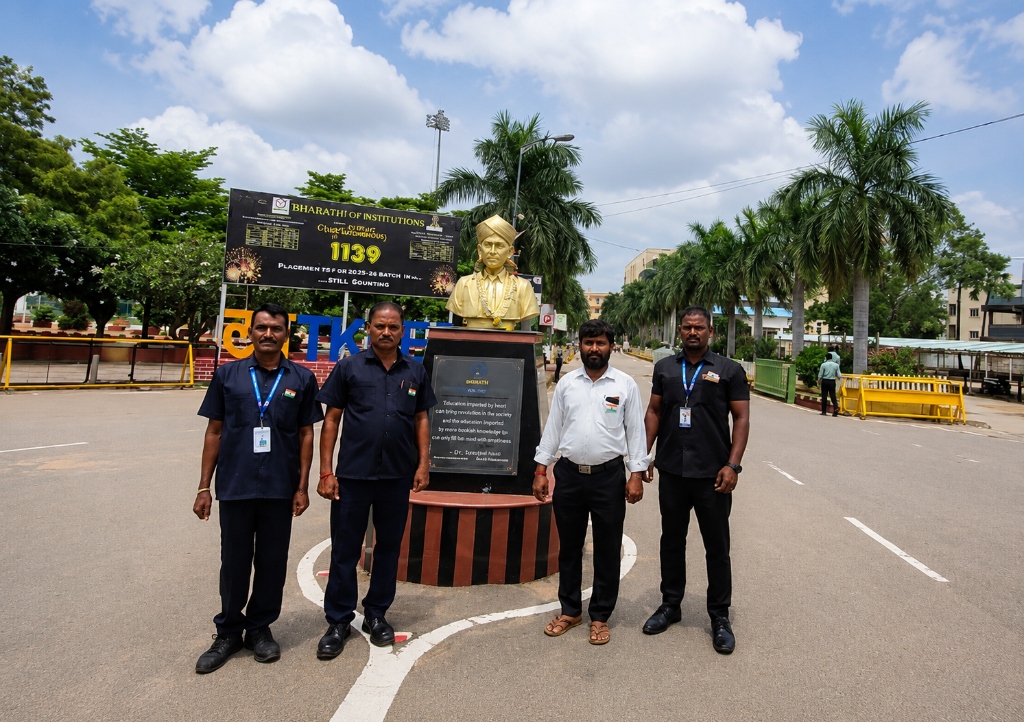 Bharathi security supervisors and field officers standing at the entrance of an institutional campus in front of a monument and placement billboard